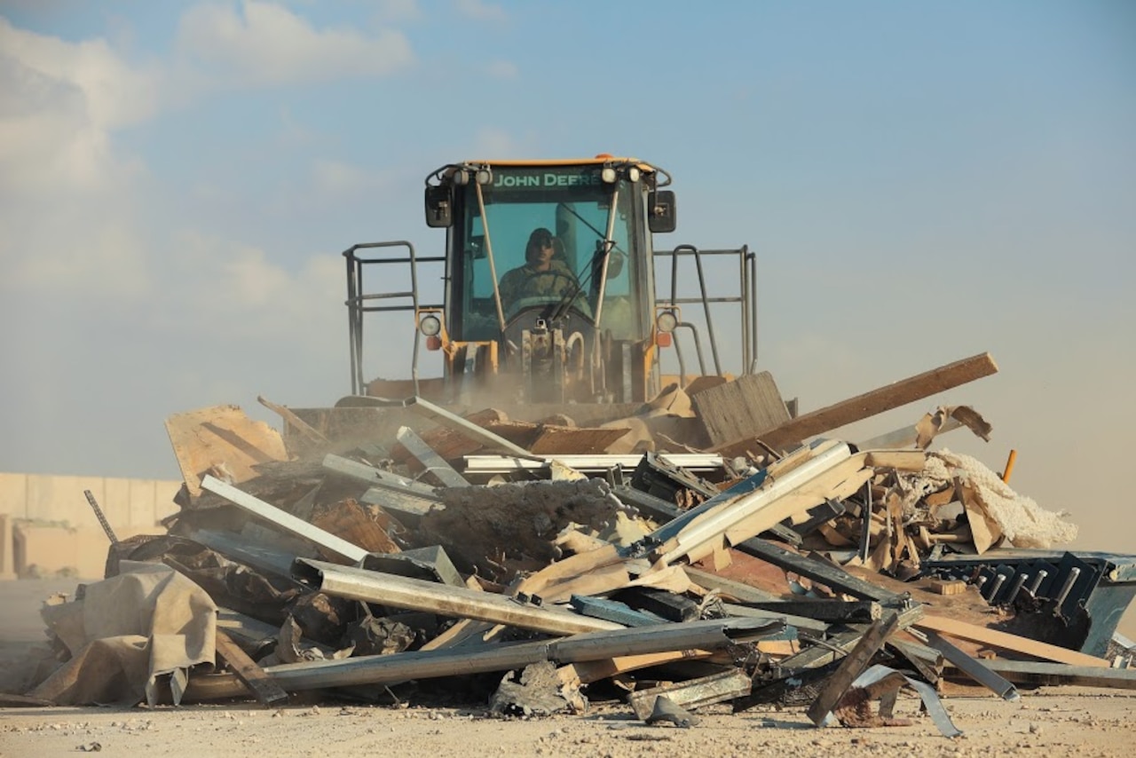 A soldier uses a bulldozer to push a pile of metal construction debris.