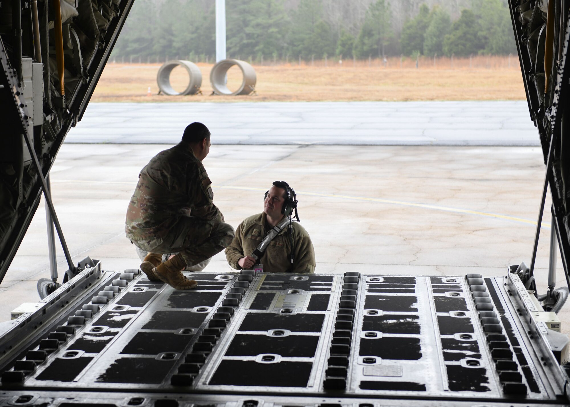 Two Airmen talk to each other in the back of a C-130.