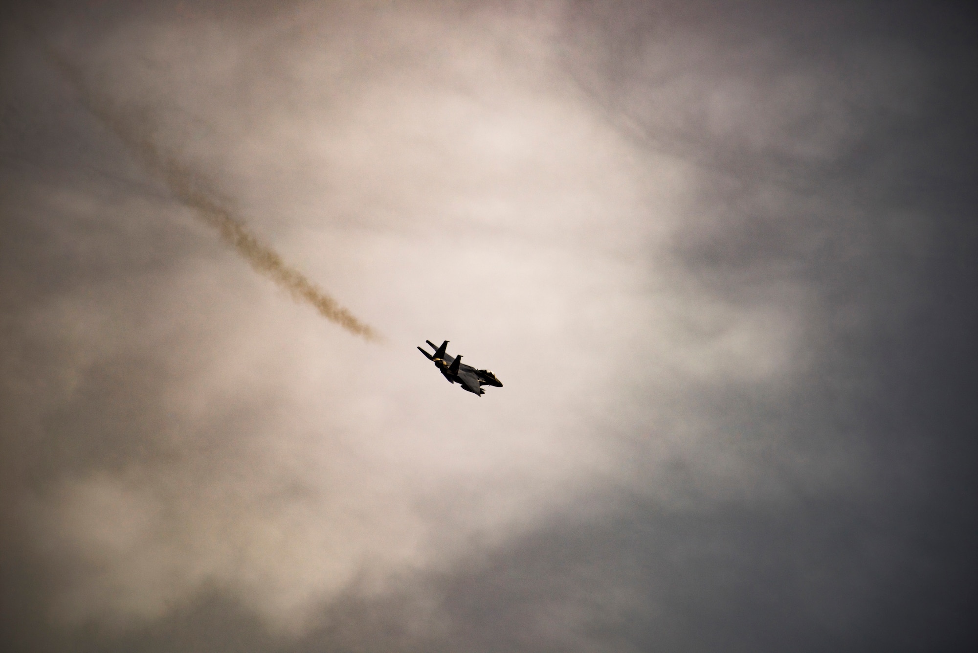 An F-15E Strike Eagle flies through overcast skies