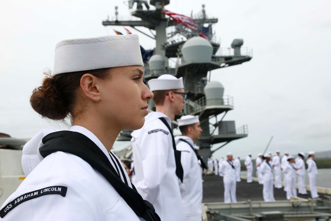 A row of sailors stand on the deck of a ship.