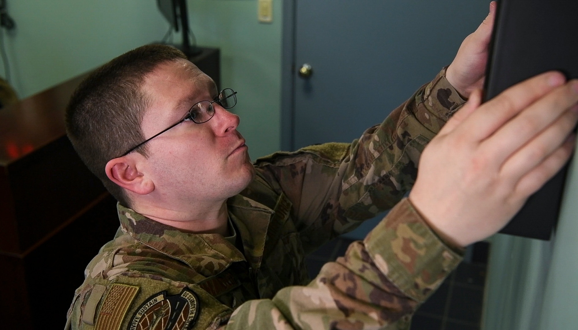 Senior Airman Matthew Chandler, 436th Logistics Readiness Squadron (LRS) ground transportation operator, places a shadow box on the wall Jan. 17, 2020, at Dover Air Force Base, Del. A memorial was built at the 436th LRS building to honor the ground transportation operators who have fallen in the line of duty. (U.S. Air Force photo by Senior Airman Christopher Quail)