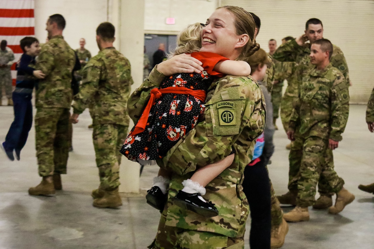 A soldier smiles brightly as she hugs her small daughter during a homecoming ceremony.