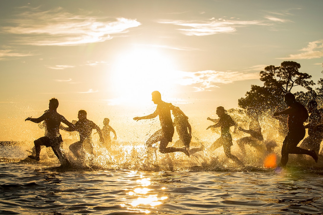 Airmen run in cold water during a sunset.