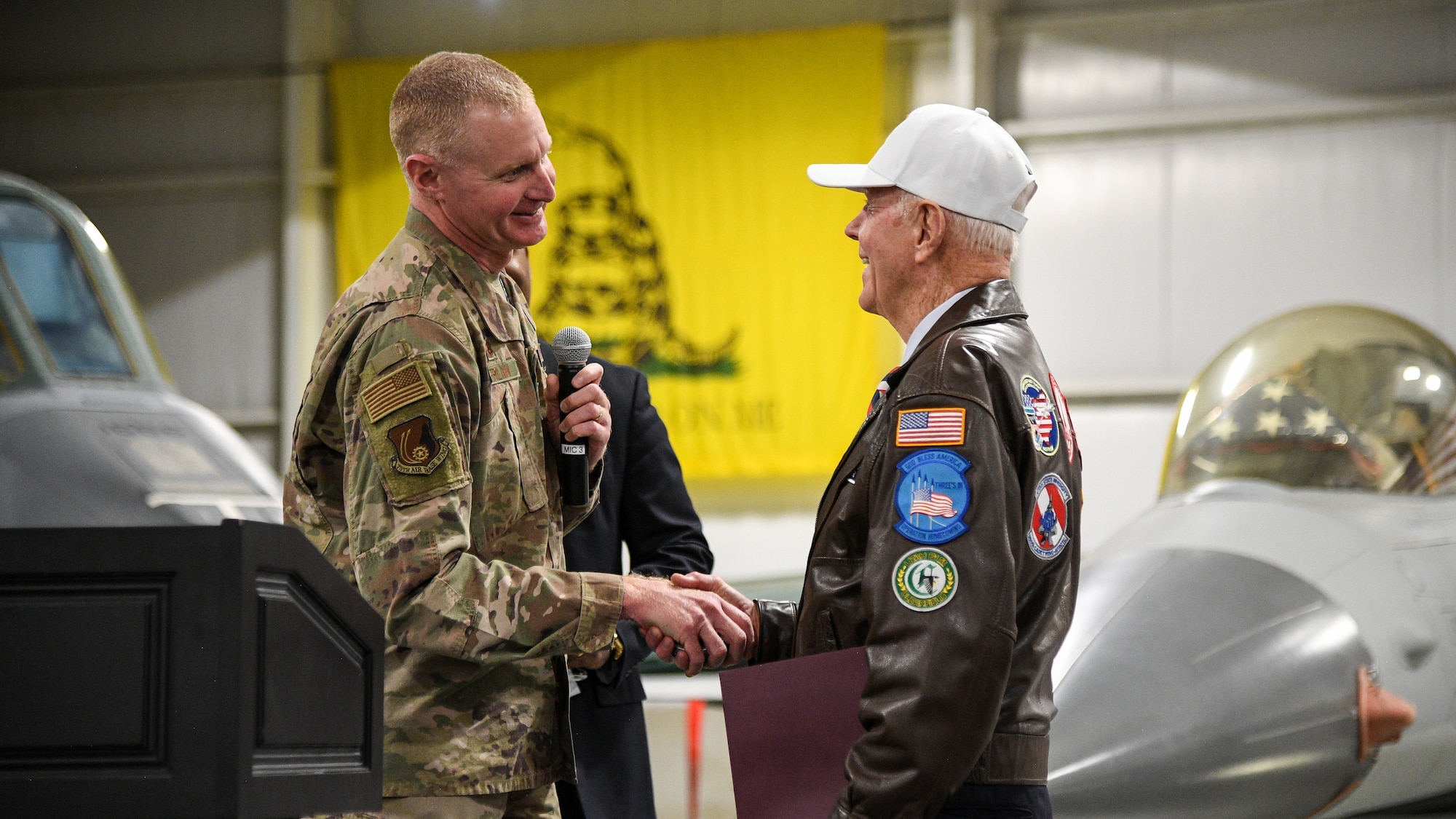 Col. Jon Eberlan at left shakes hands with retired Air Force Lt. Col. Jay Hess. Images of aircraft in the museum appear int he background.