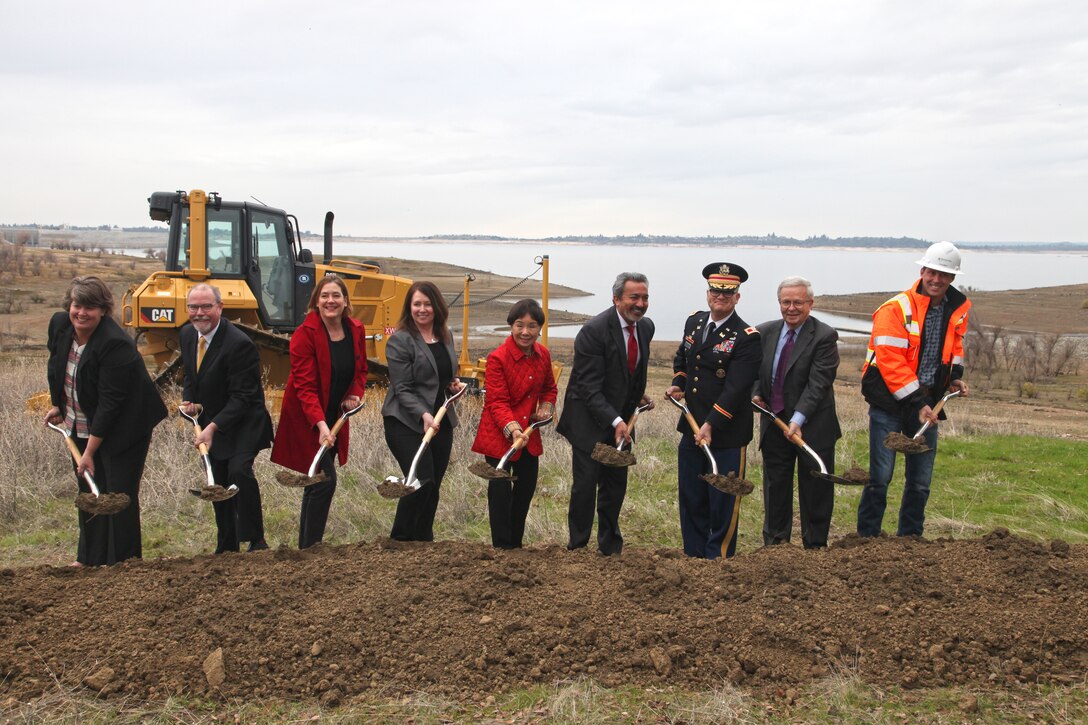 men and women hold shovels of dirt in a field