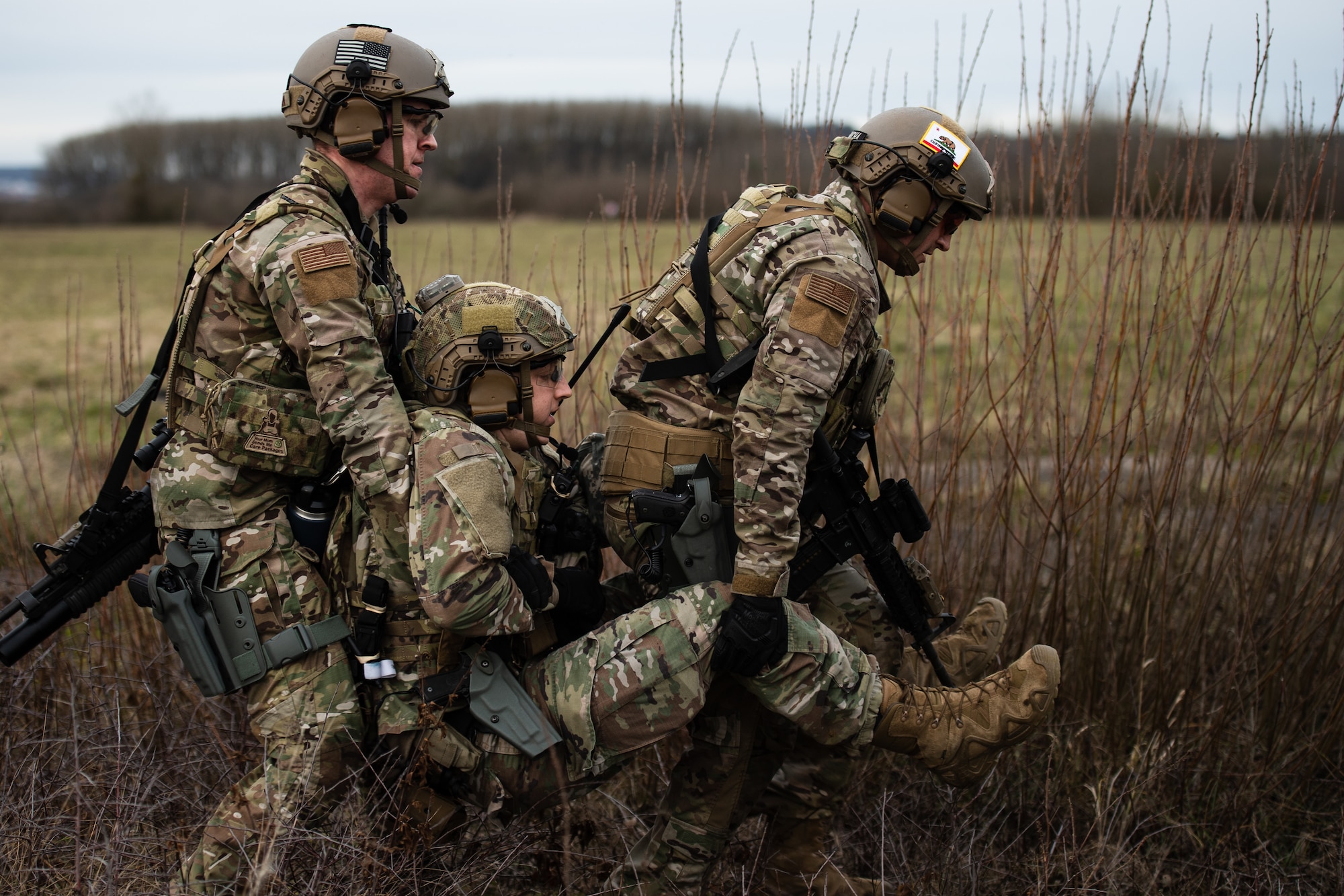 U.S. Air Force Staff Sgt. Dillion Rickman, 435th Security Forces Squadron vehicle maintainer, left, and Staff Sgt. Esteban Goniwicha, 435th SFS ground combat readiness training center instructor, right, lift Staff Sgt. Collin Braun, 435th SFS resource advisor, during exercise Frozen Defender in Grostenquin, France, Jan. 14, 2020. Frozen Defender tests the squadron’s capabilities in a contested environment under harsh conditions. The exercise provided opportunities for the Defenders to use various skillsets to complete their mission including self-aid and buddy care, vehicle disablement, and building clearing. (U.S. Air Force photo by Staff Sgt. Devin Boyer)