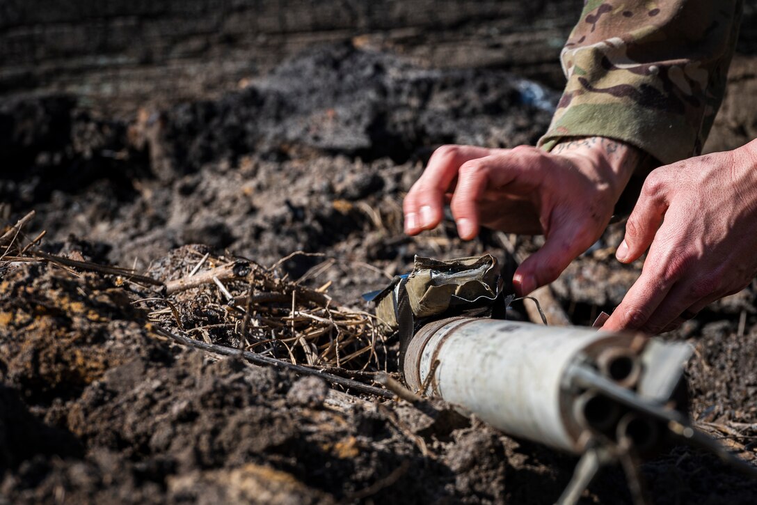 A photo of an Airman placing plastic explosive on a UXO