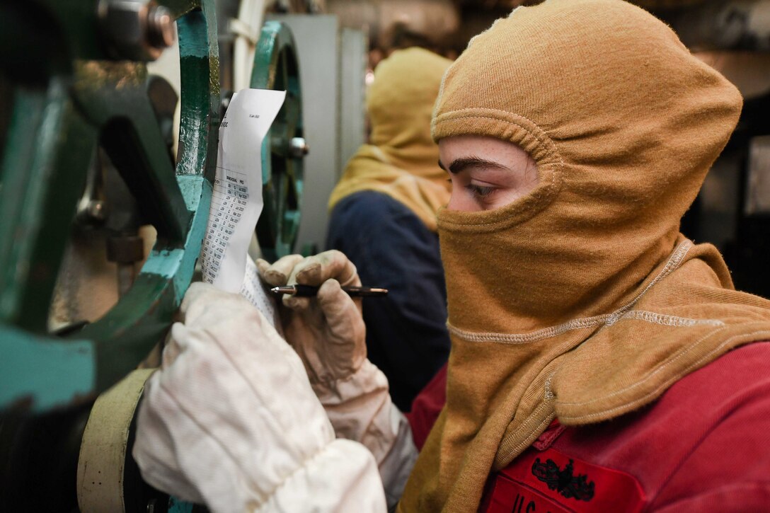 A sailor with a mask and gloves on writes on a paper.