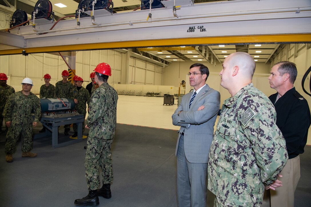 Defense Secretary Dr. Mark T. Esper stands with service members in a large building.