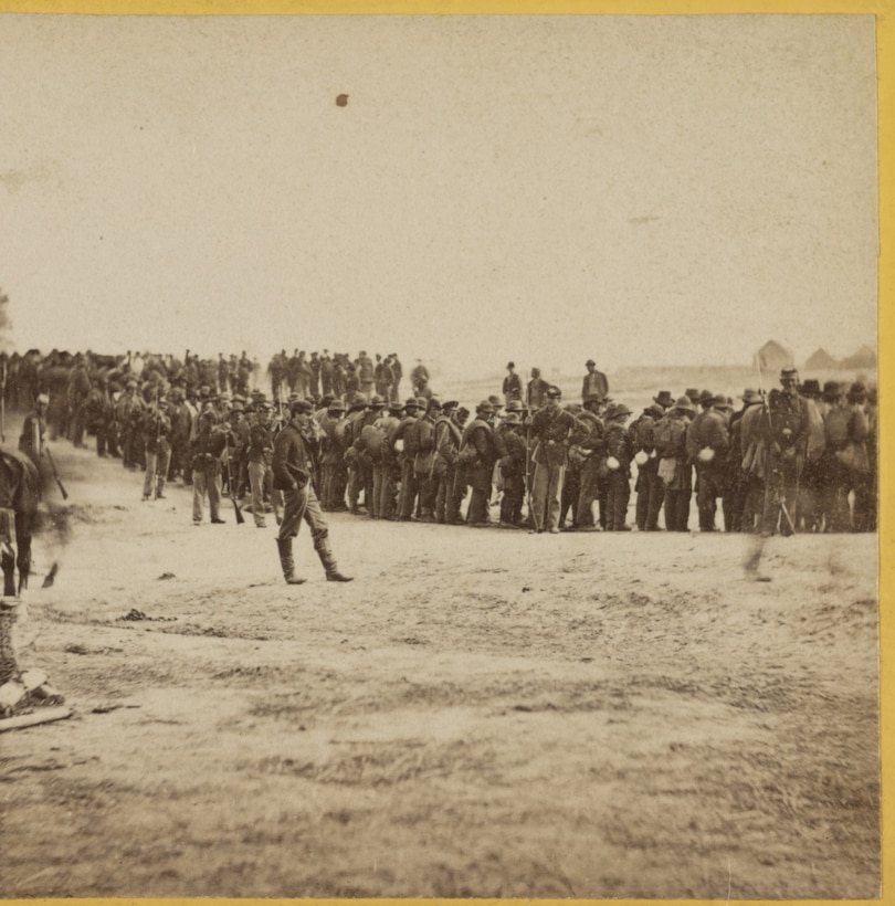 Civil War soldiers stand in a line on a barren field.