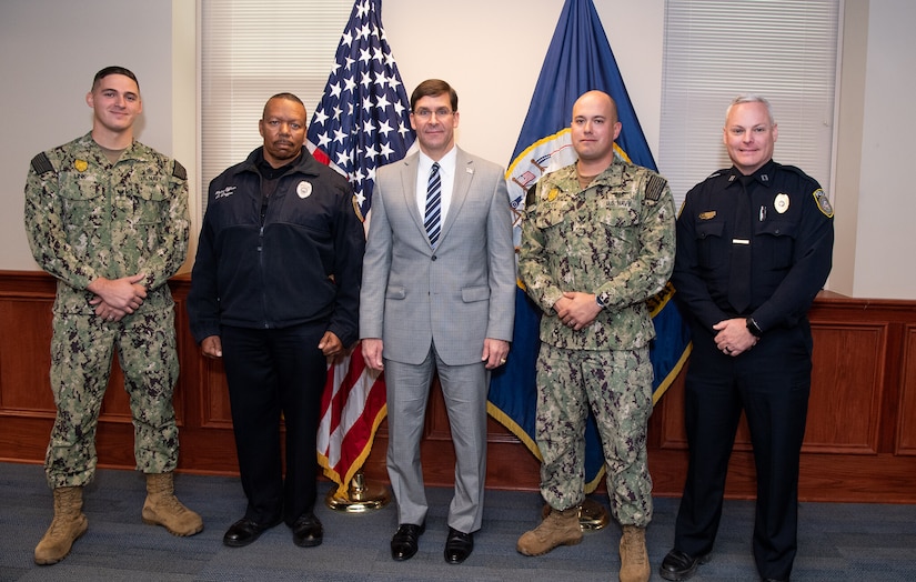 Five men stand side by side in front of an American flag and a U.S. Navy flag.