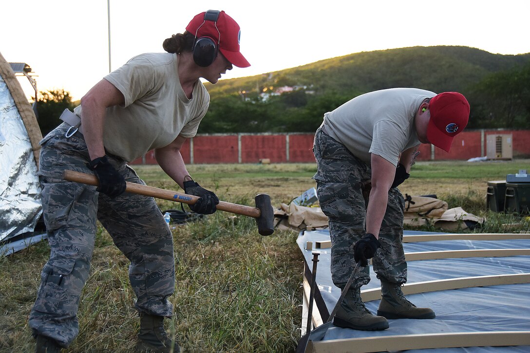 Two service members hammer stakes into the ground as they set up tents.