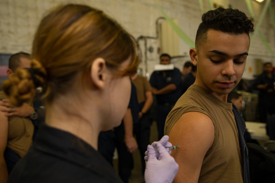 Navy Hospital Corpsman 3rd Class Kindal Kidd, assigned to USS Gerald R. Ford's medical department, administers a flu shot to a sailor in the ship's hangar bay.