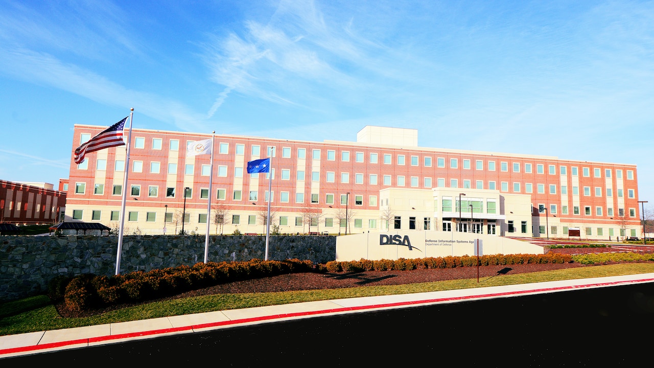 A brick building sits under a blue sky.  In front, a wall is inscribed with “DISA” and “Defense Information Systems Agency.”