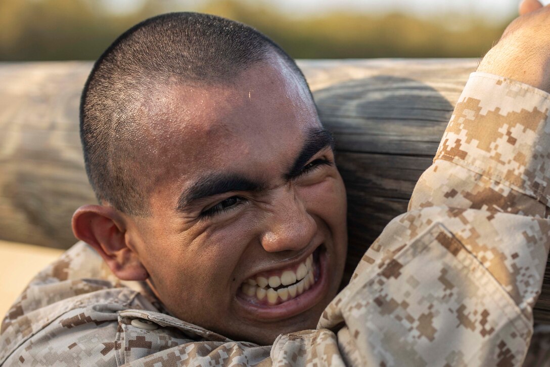 A Marine Corps recruit carries a log over his shoulder.