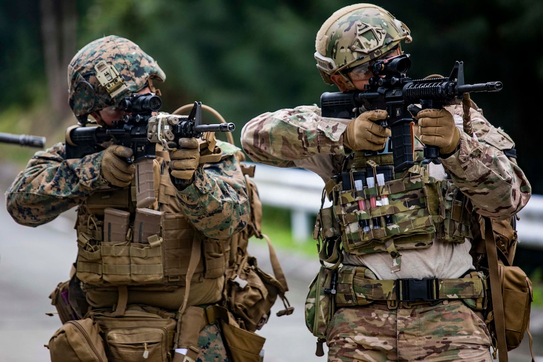 A Marine and an airman stand side by side holding up their weapons.