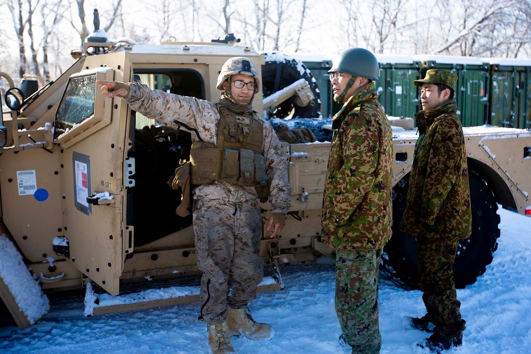A Marine stands outside of a vehicle while talking to two Japanese soldiers.