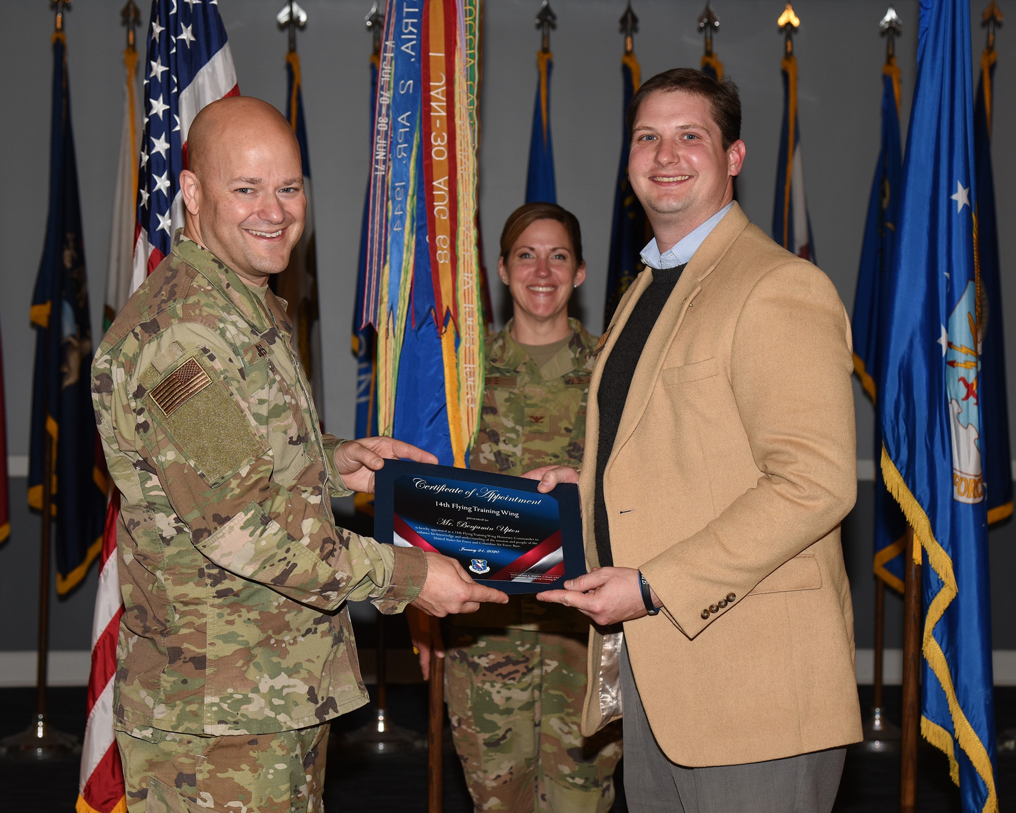 Col. Samantha Weeks (center), 14th Flying Training Wing commander, smiles as Chief Master Sgt. Trevor James (left), 14th FTW command chief, gives a certificate to an honorary commander inductee on Jan. 21, 2020, at Columbus Air Force Base, Miss. As honorary commanders, local leaders will be fully immersed in the Air Force culture and experience the wing’s mission of cultivating, creating pilots and connecting first hand. (U.S. Air Force photo by Elizabeth Owens)