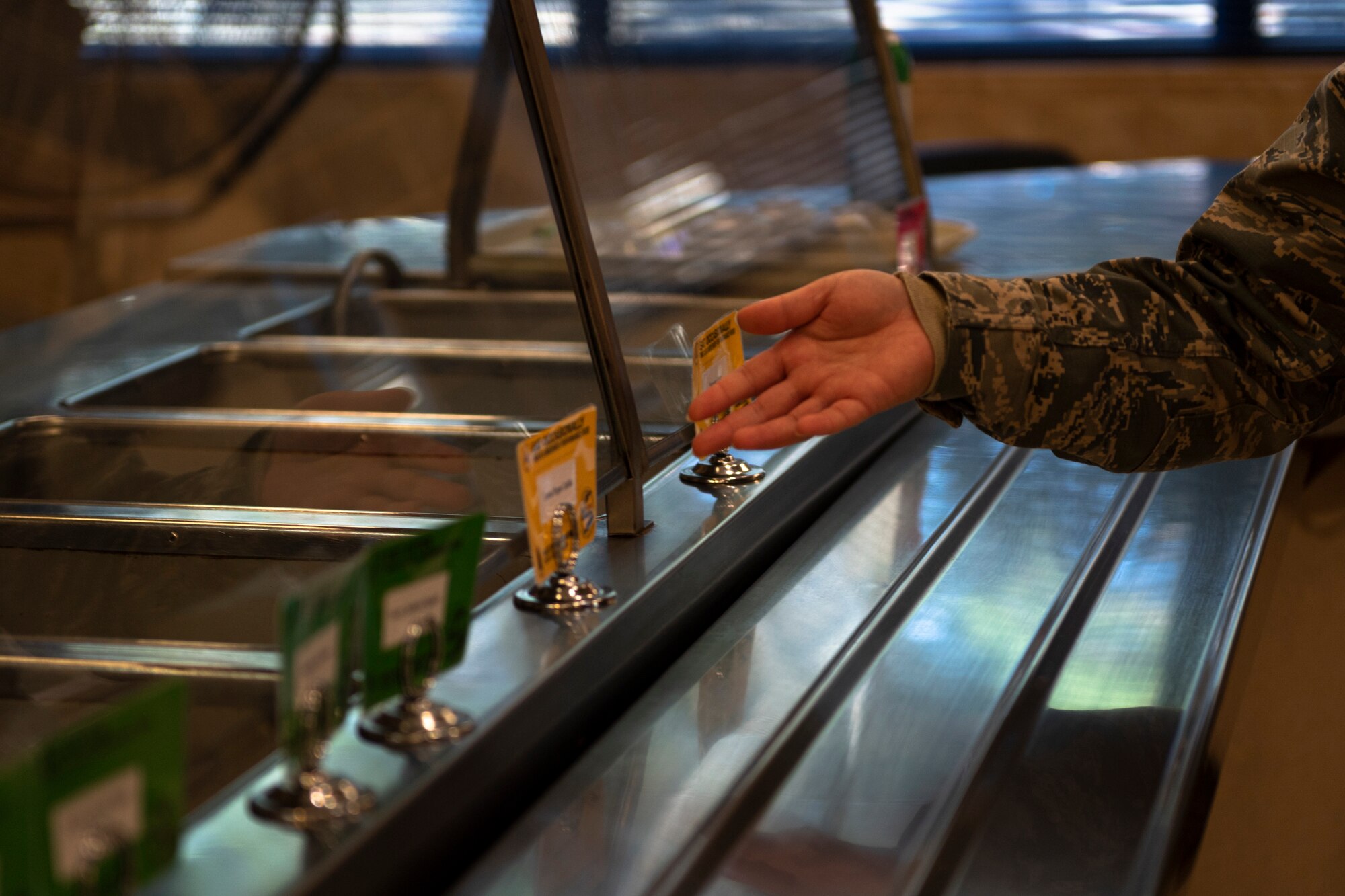 A photo of an Airman pointing to signs on the food line at the dining facility