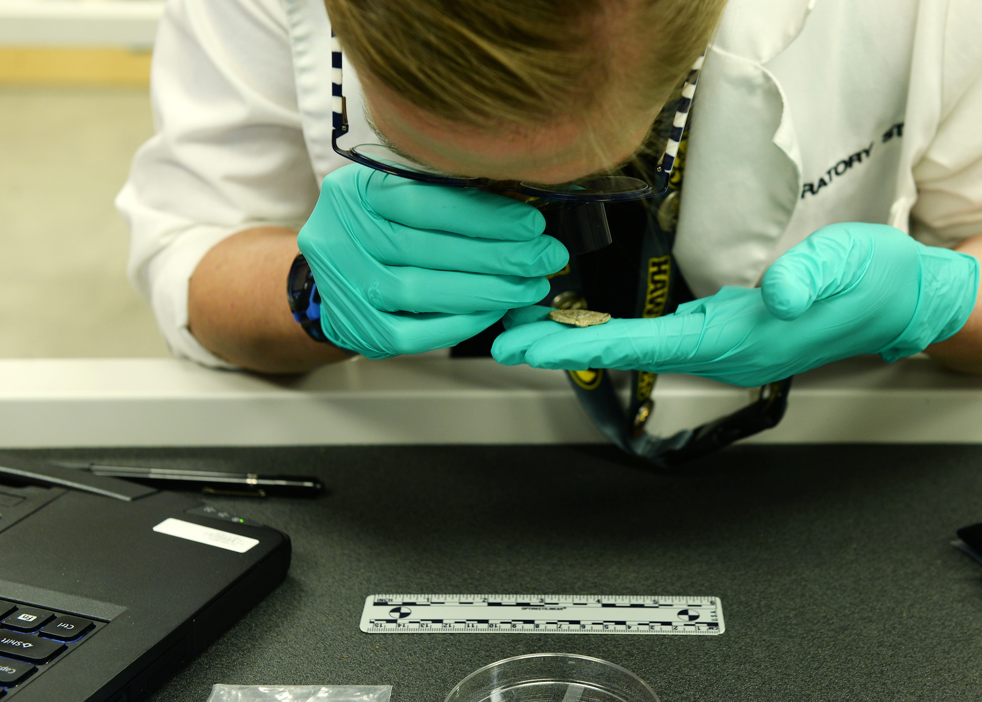 A doctor in a laboratory examines material evidence with a hand held magnifying glass.