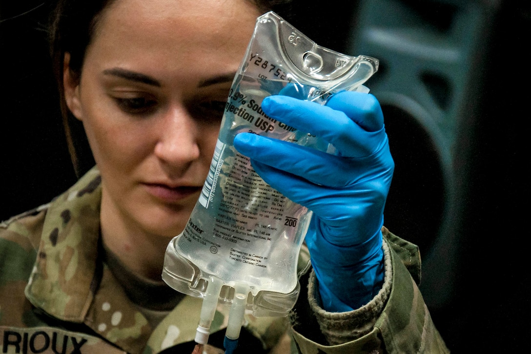 A soldier looks at a medical saline bag in her hand.