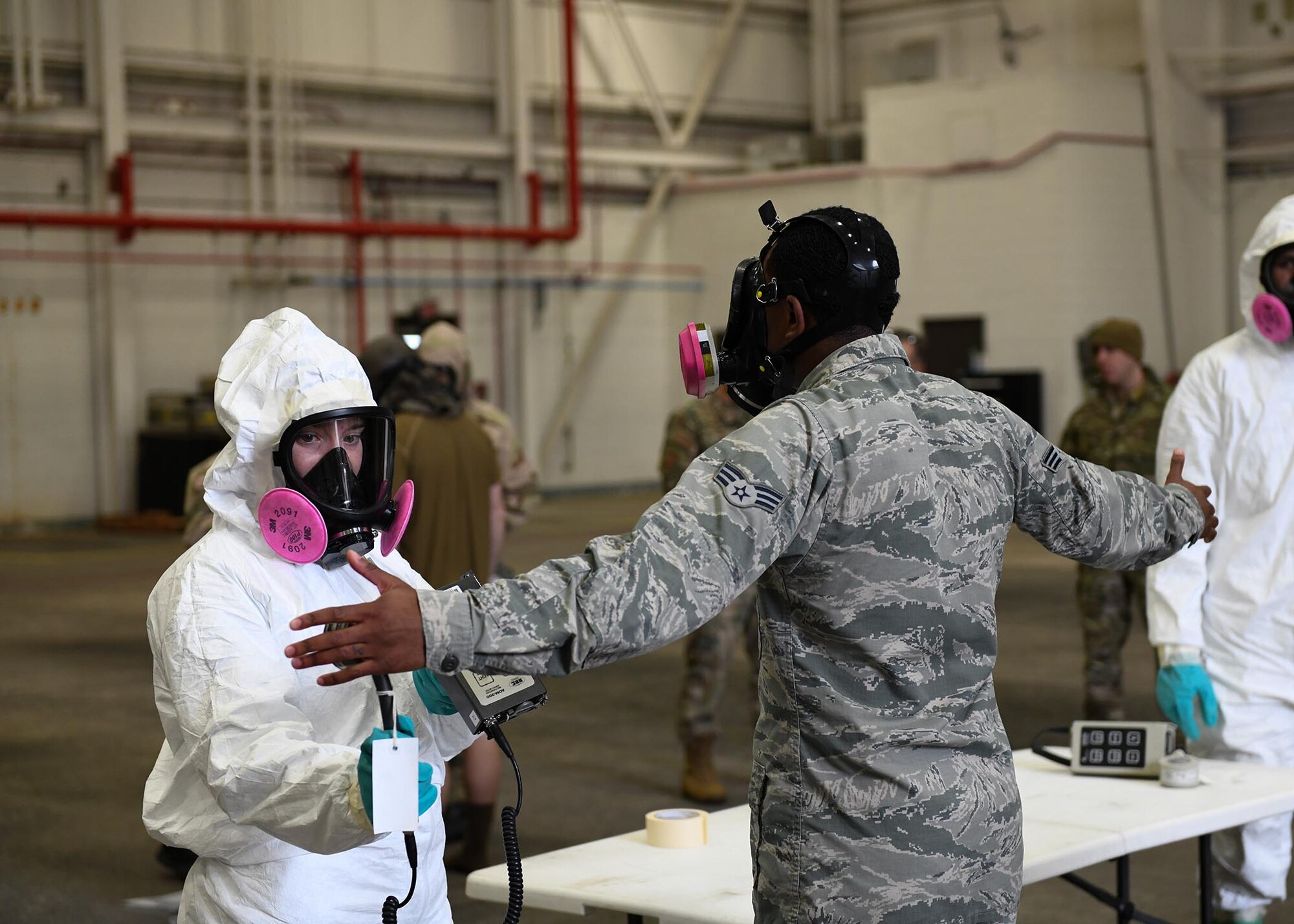 An Airman checks another Airmen for simulated radiation using a small grey tool.