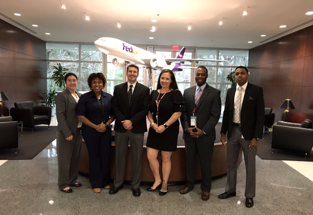 Three women and three men stand in front of a Fedex model plane.
