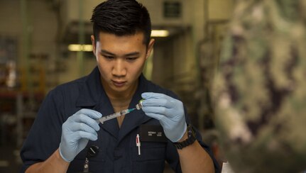 Seaman Kenny Liu, a Navy hospital corpsman assigned to USS Gerald R. Ford's medical department, prepares a needle with a flu vaccination in the ship's hangar bay.