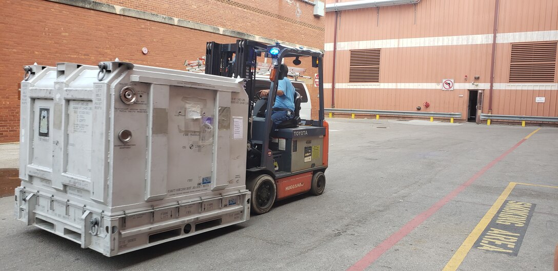 A man on a forklift moves metal storage containers.