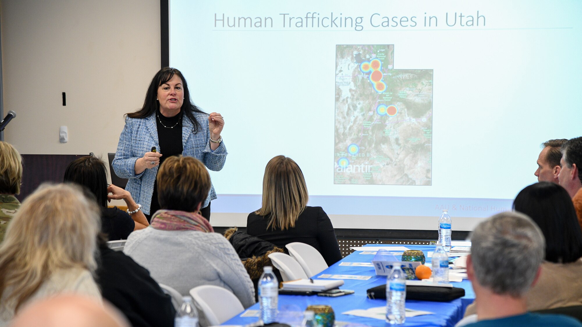Allison Smith, education and outreach specialist for the Trafficking in Persons Program with the Refugee and Immigrant Center in Salt Lake City, stands in front of a screen depicting human trafficking hot spots across the state of Utah. Audience members look on in the foreground.