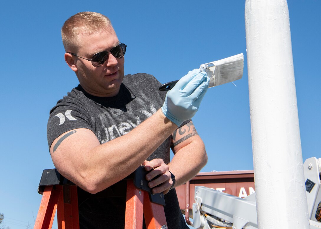 United States Air Force Master Sgt. Adlai Barber, 325th Maintenance Squadron, non-commissioned officer in charge of low observables, applies primer to the base of a flag pole, Panama City, Florida, Jan. 25, 2020. Barber along with three airmen volunteered to restore the St. Andrew School flag pole that became rusted over after Hurricane Michael.