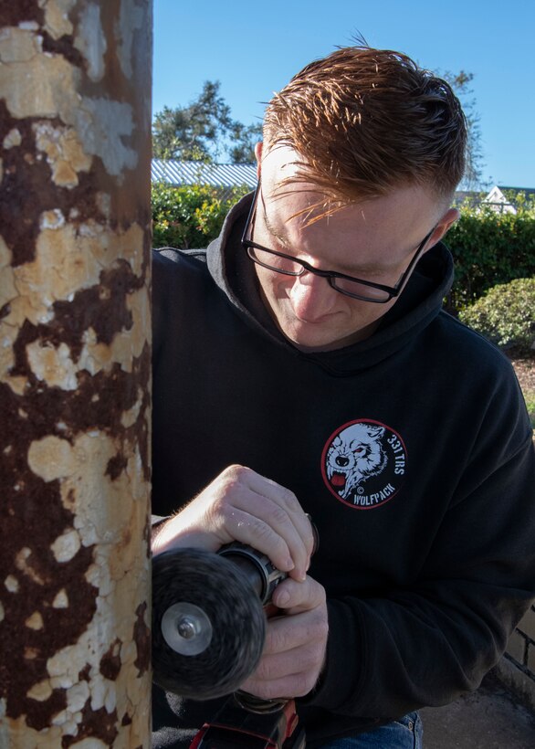 United States Air Force Airman 1st Class Bailey McDonald, 325th Maintenance Squadron, low observable maintainer, sands rust off the base of a flag pole, Panama City, Florida, Jan. 25, 2020. McDonald and his fellow airmen volunteered more than three hours sanding, priming and painting the St. Andrew School flag pole that was rusted after Hurricane Michael.