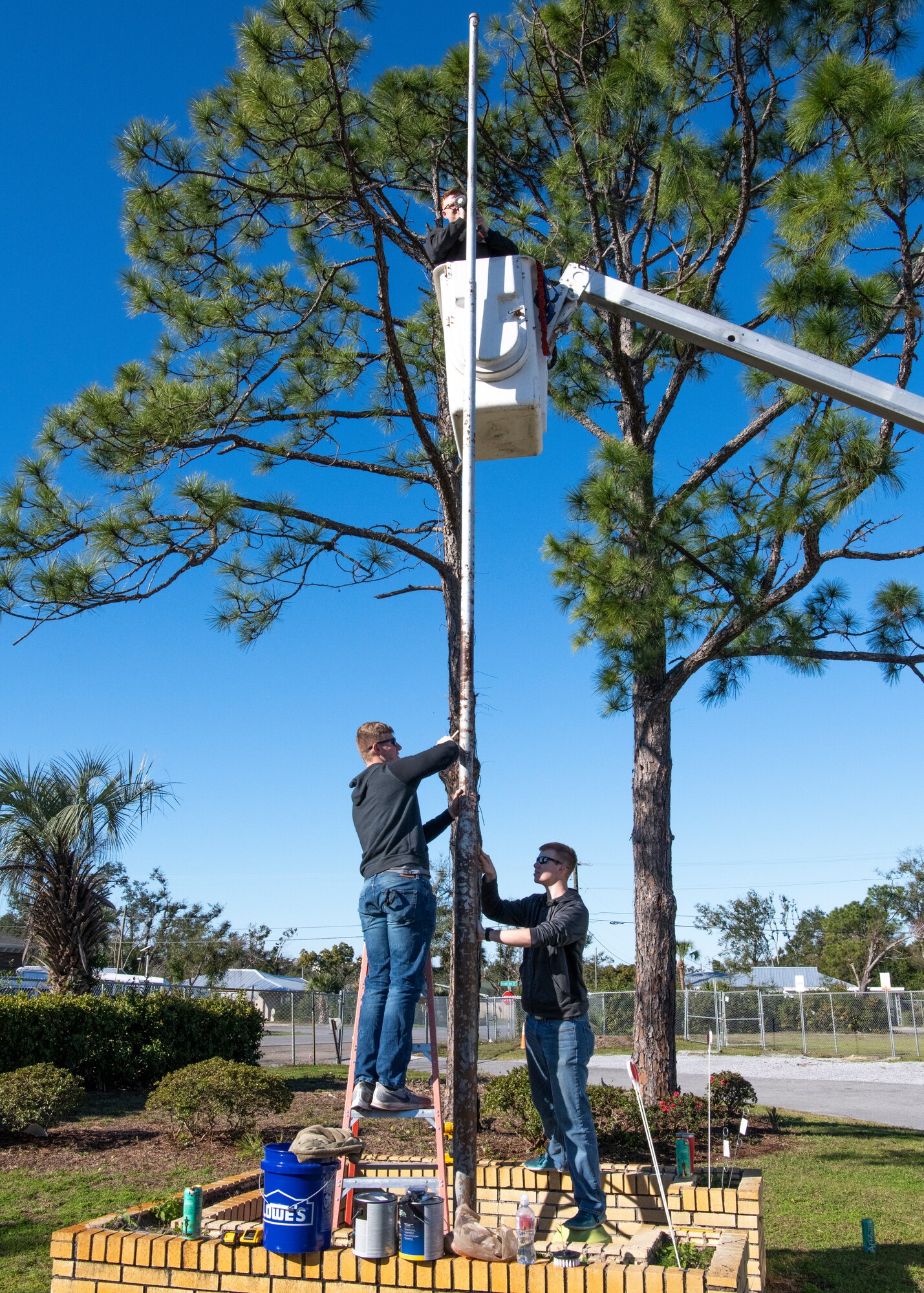 United States Air Force Staff Sgt. Erich Olsen (left), Airman 1st Class William Kretzer (right), and Airman 1st Class Bailey McDonald (top), 325th Maintenance Squadron, low observable maintainers, sand rust off of a flag pole, Panama City, Florida, Jan. 25, 2020. The airmen volunteered to restore the St. Andrew School flag pole that became rusted over after Hurricane Michael.