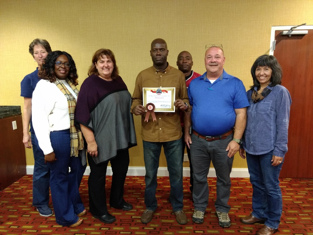 South-East Deputy Director Audrey Weber (far left) helps present the third place award to (from left to right) Centralized Demil Division Warehouse Supervisor La Toya Smith, CDD Operations Supervisor Gail Haas-Sibley, Area Manager Reggie McFadden, CDD Warehouse Supervisor Nathaniel Smith and Site Supervisor Alan Wilkey along with South-East Director Kathy Atkins-Nuñez (far right).