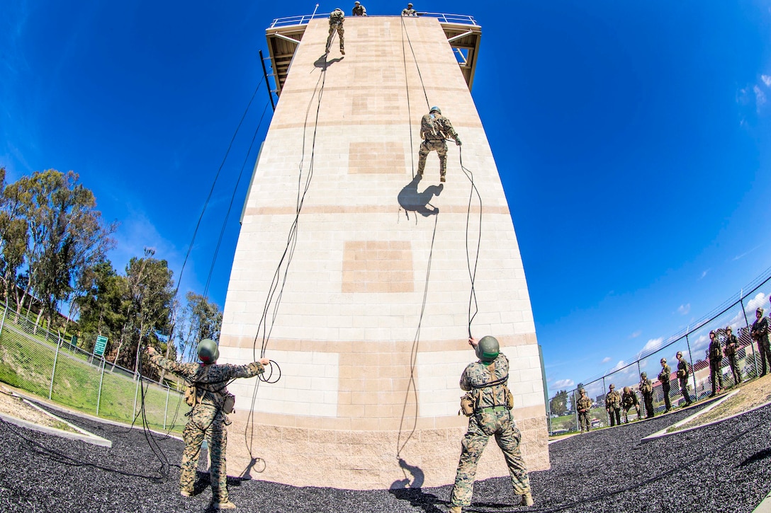 Marines rappel down the side of a wall.