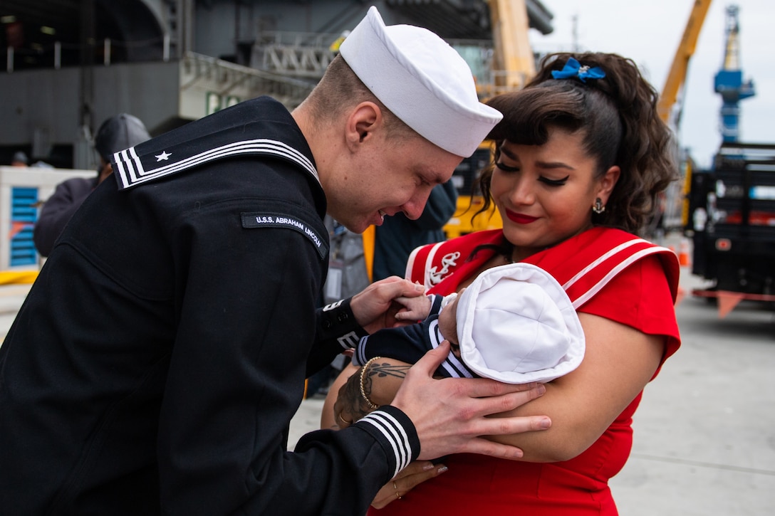 A sailor looks at his baby held by a woman.