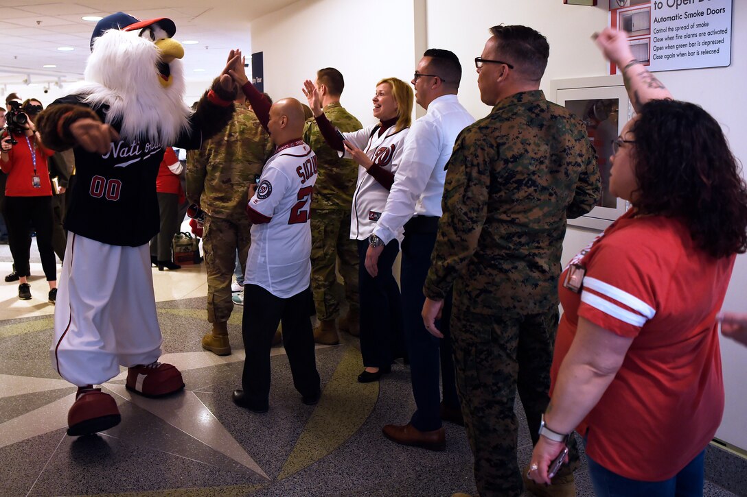 Civilians and military personnel line up in a hallway in the Pentagon. A person in a large bird costume slaps a high-five with a man.