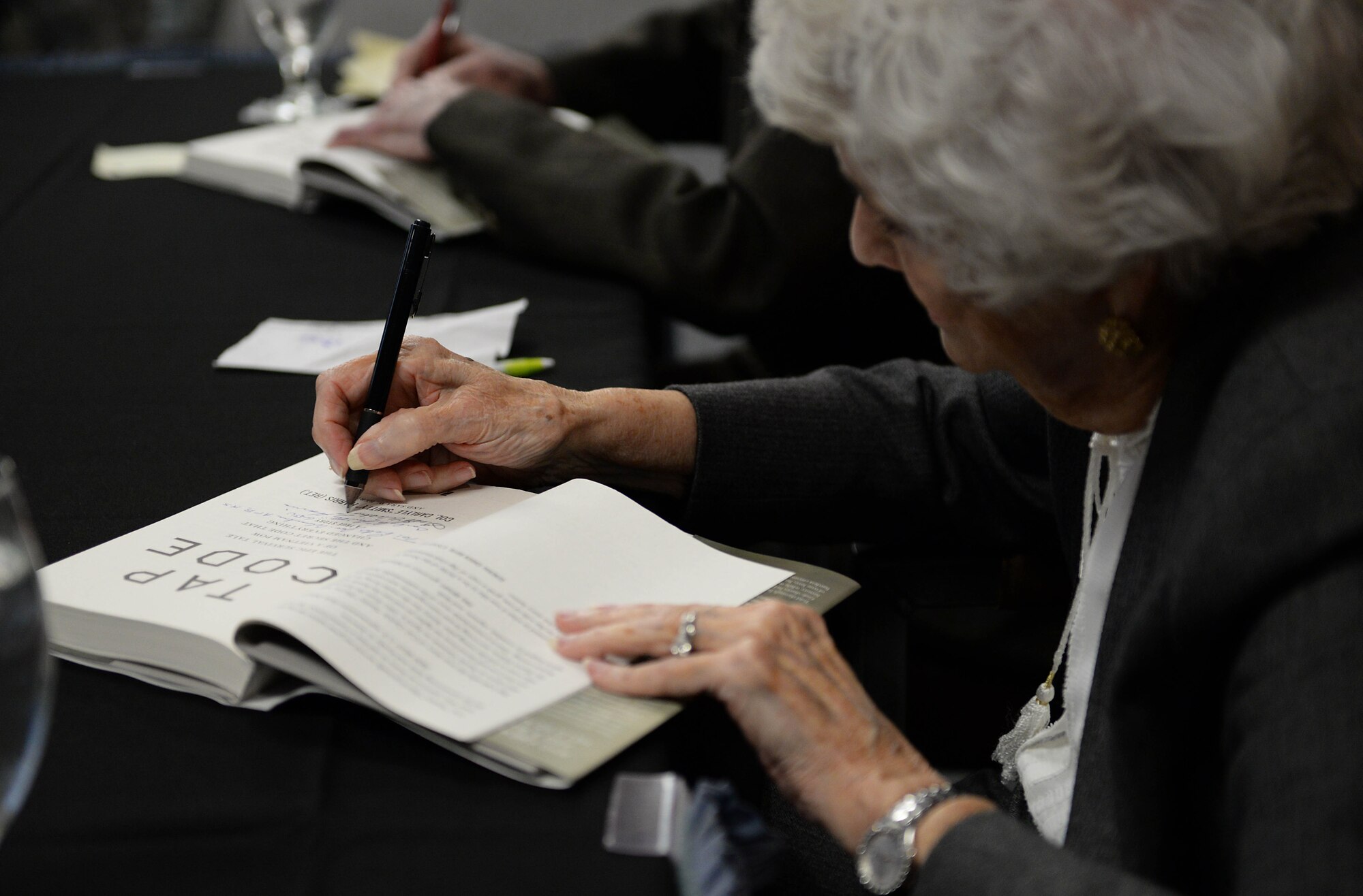 Louise Harris, wife of Retired Air Force Col. Carlyle “Smitty” Harris, signs her name during a book signing Jan. 10, 2020, at the Columbus Event Center on Columbus Air Force Base, Miss. The book, written from the perspectives of Smitty and Louise, shares never-before-told details of underground operations during the Vietnam War while showcasing a true story of having the strength, dignity and resolve necessary to endure challenging circumstances. (U.S. Air Force photo by Airman 1st Class Hannah Bean)