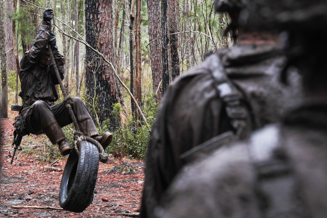 A Marine recruit stands on a tire swing as other recruits watch.