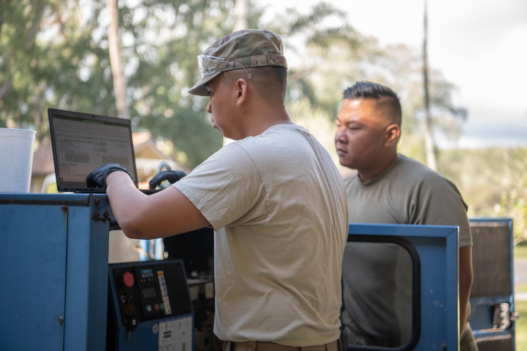 U.S. Air Force Staff Sgt. Gabriel Carias, 624th Civil Engineer Squadron electrical power production craftsman, fills out a maintenance log for an electrical generator while Tech. Sgt. Jordan Balangue, 624th CES electrical power production craftsman, monitors the performance of the generator at Bellows Air Force Station, Hawaii, Jan. 25, 2020.