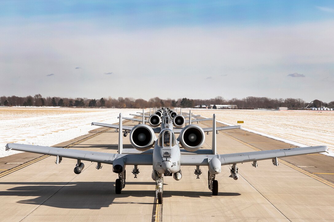 Military aircraft line up behind each other on a runway.