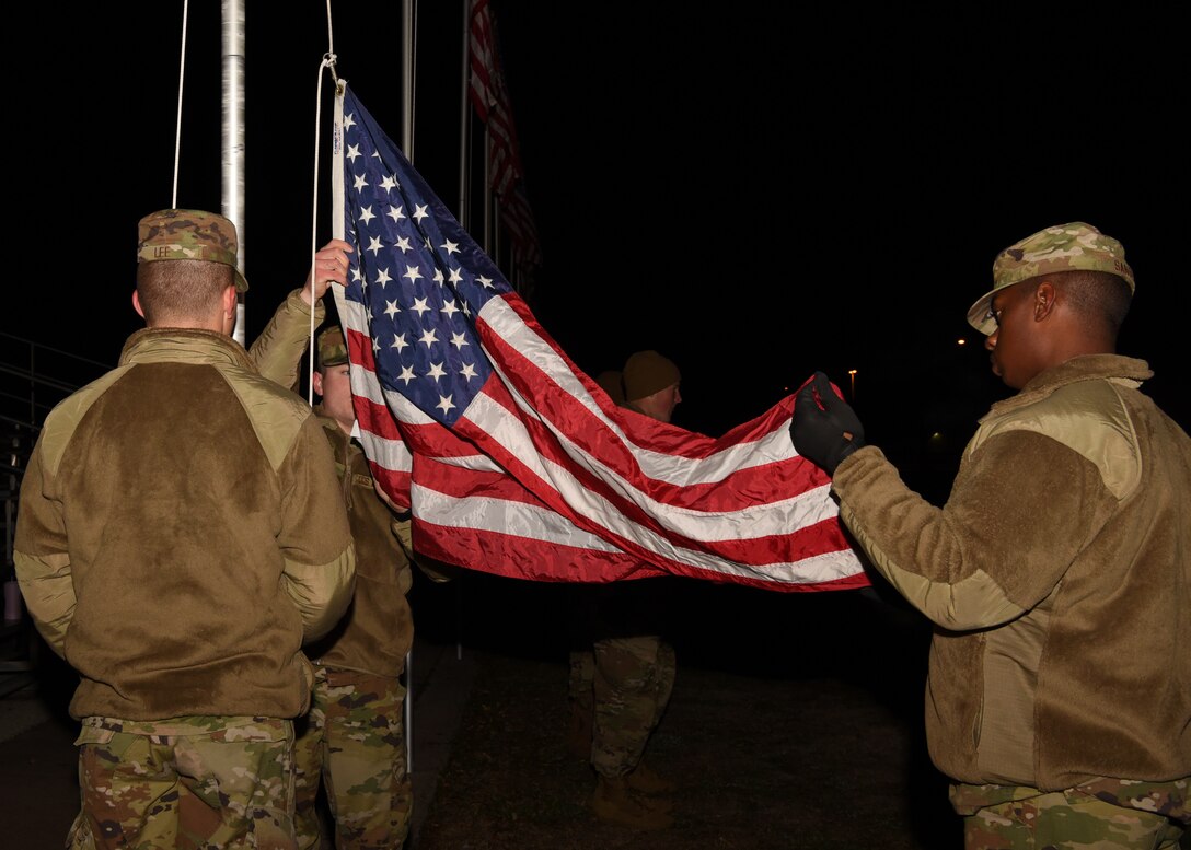 U.S. Air Force fire protection students from the 312th Training Squadron work as a team to raise an American flag before sunrise on the parade field at Goodfellow Air Force Base, Texas, Jan. 24, 2020. These students volunteered their help with the flag detail before their technical training course starts.  (U.S. Air Force photo by Airman 1st Class Abbey Rieves)
