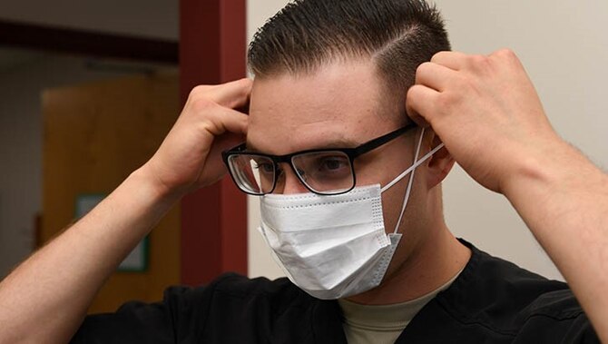 A dental assistant with the 319th Medical Group, demonstrates proper sanitary procedure by putting on a face mask at the medical treatment facility at Grand Forks Air Force Base, North Dakota.
