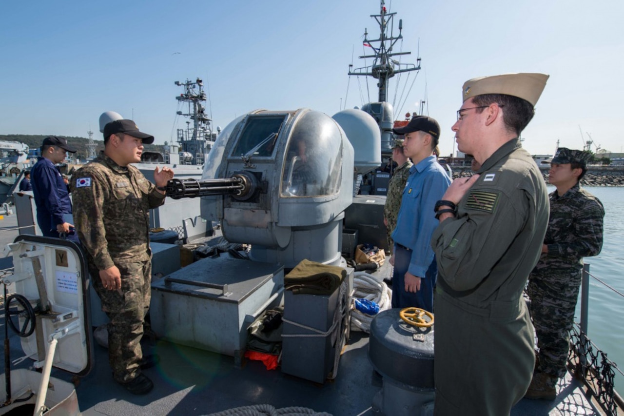 Men in military uniforms stand on the deck of a ship.