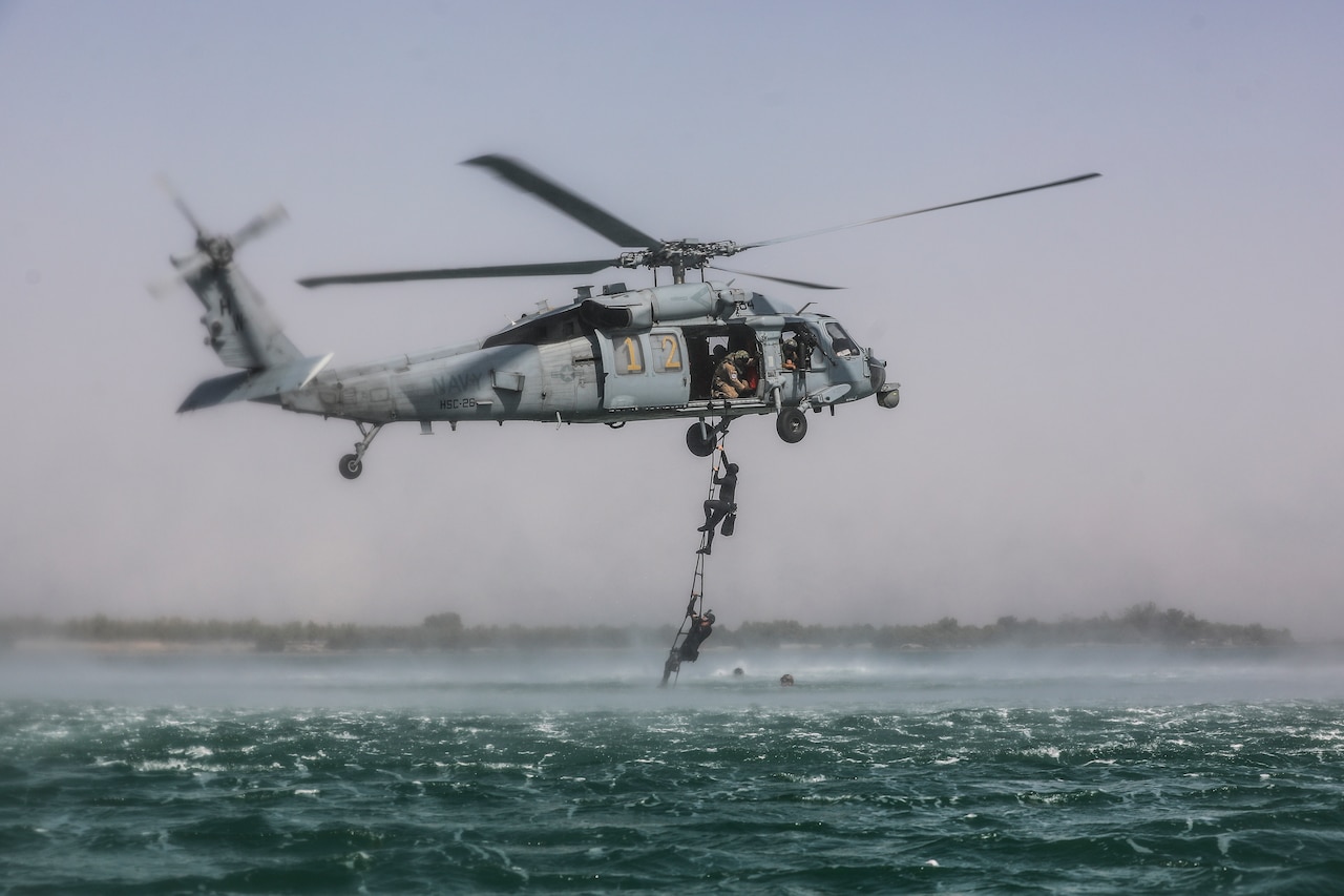 Soldiers climb out of sea into a Navy helicopter.