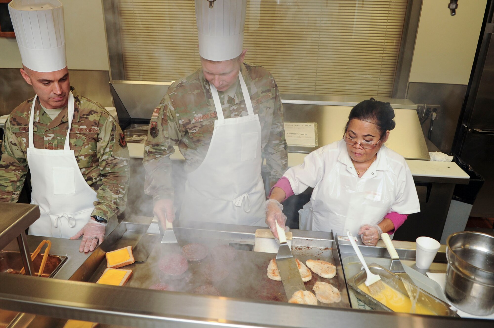 Senior MSgt. Joseph Gibson (left), Air and Space Intelligence Group superintendent, Chief MSgt. Randy Novobilski, Geospatial and Signatures Intelligence Group superintendent and Jude Dantzler, Pitsenbarger Dining Facility line cook, grill food at the Pitsenbarger Dining Facility on Wright-Patterson Air Force Base, Ohio on Jan. 24, 2020.  Dantzler, who has worked at the facility four years, assisted a team of National Air and Space Intelligence Center group commanders, superintendents and first sergeants with preparing and serving food for junior enlist Airmen as a means to raise morale and foster open communication.  (U.S. Air Force photo Staff Sgt. Seth Ray Stang)