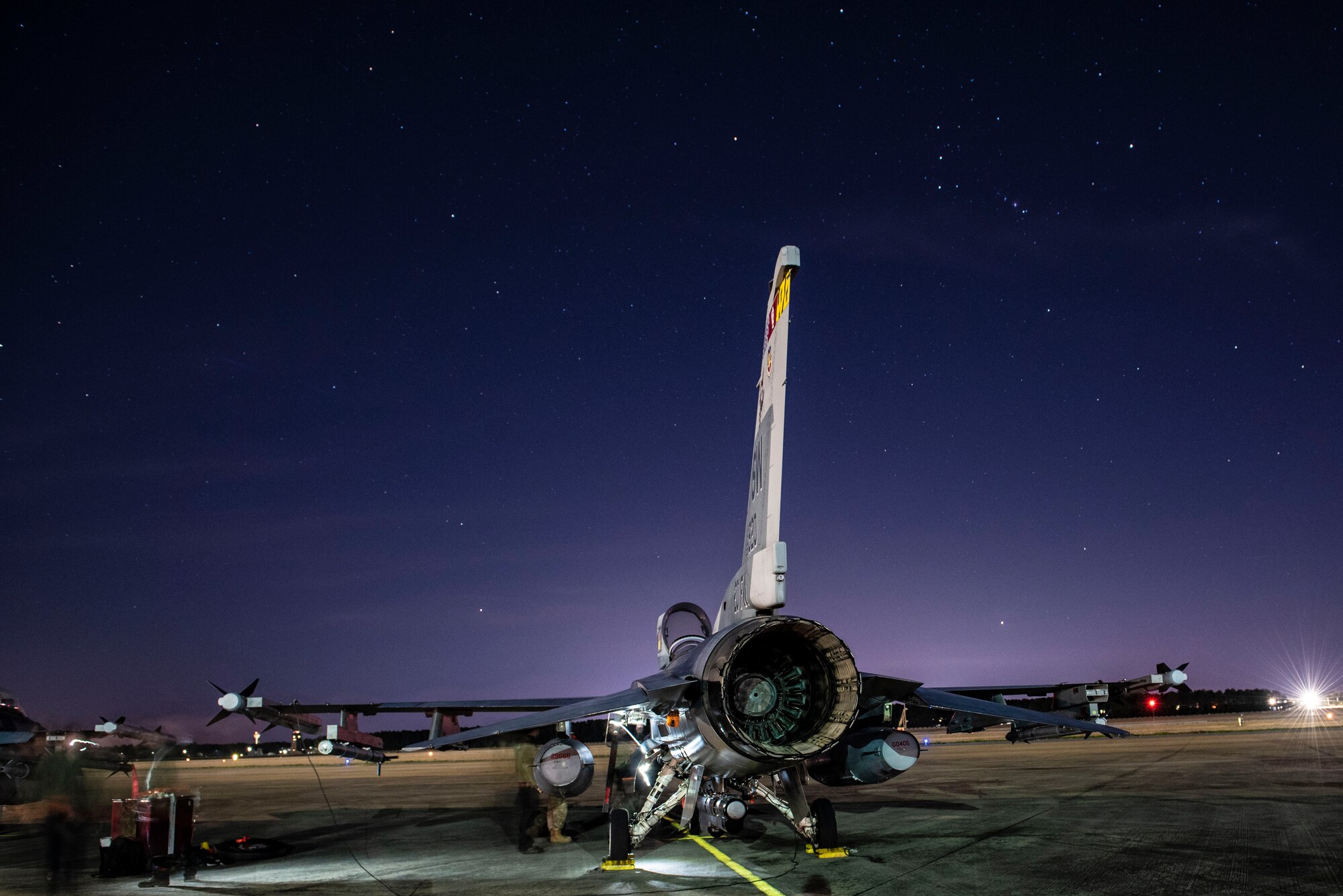 A photo of an F-16 at night with maintainers working on it.