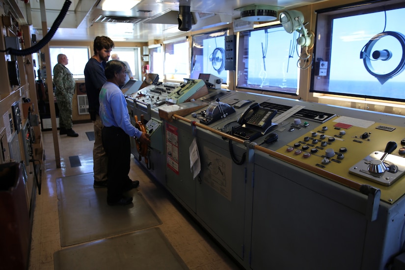 Two individuals man the controls of a naval vessel.
