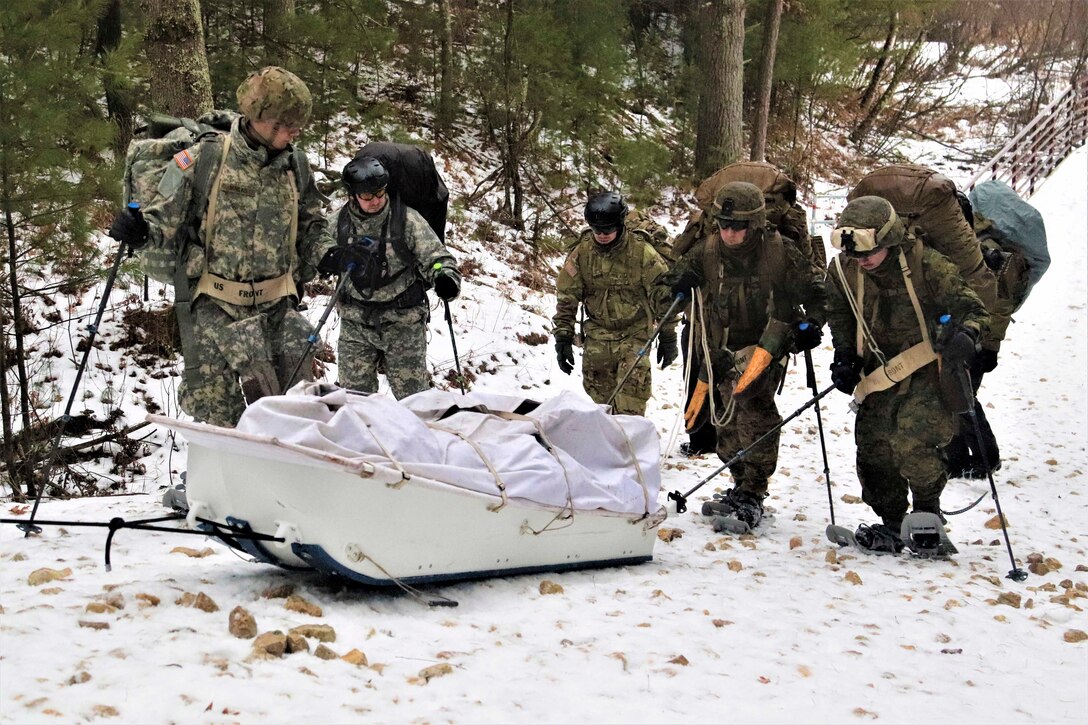 A group of soldiers move through the snow and terrain on snowshoes.