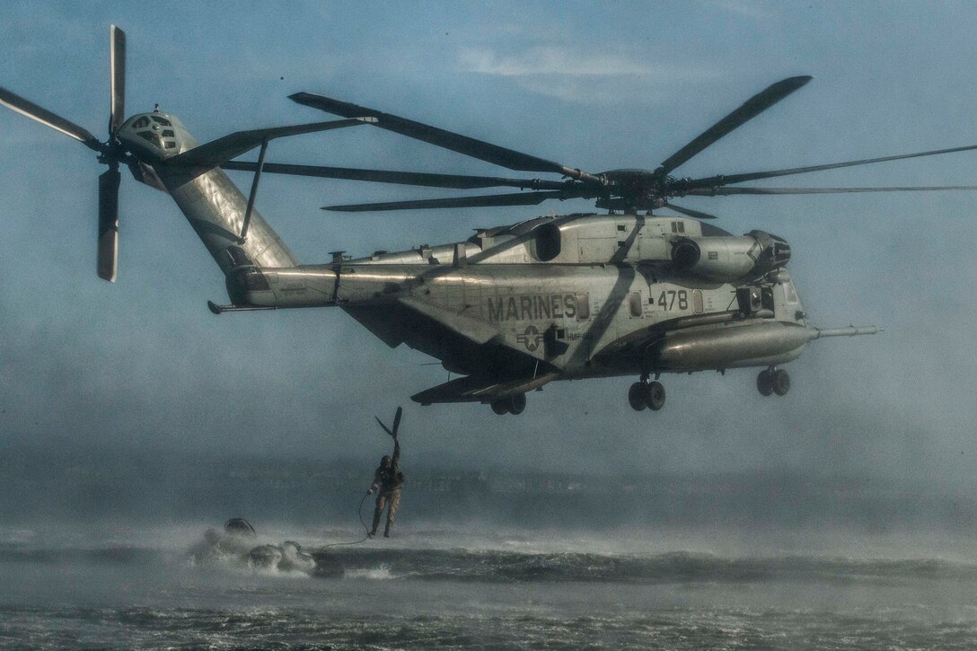 A Marine jumps from a large helicopter hovering over the ocean.